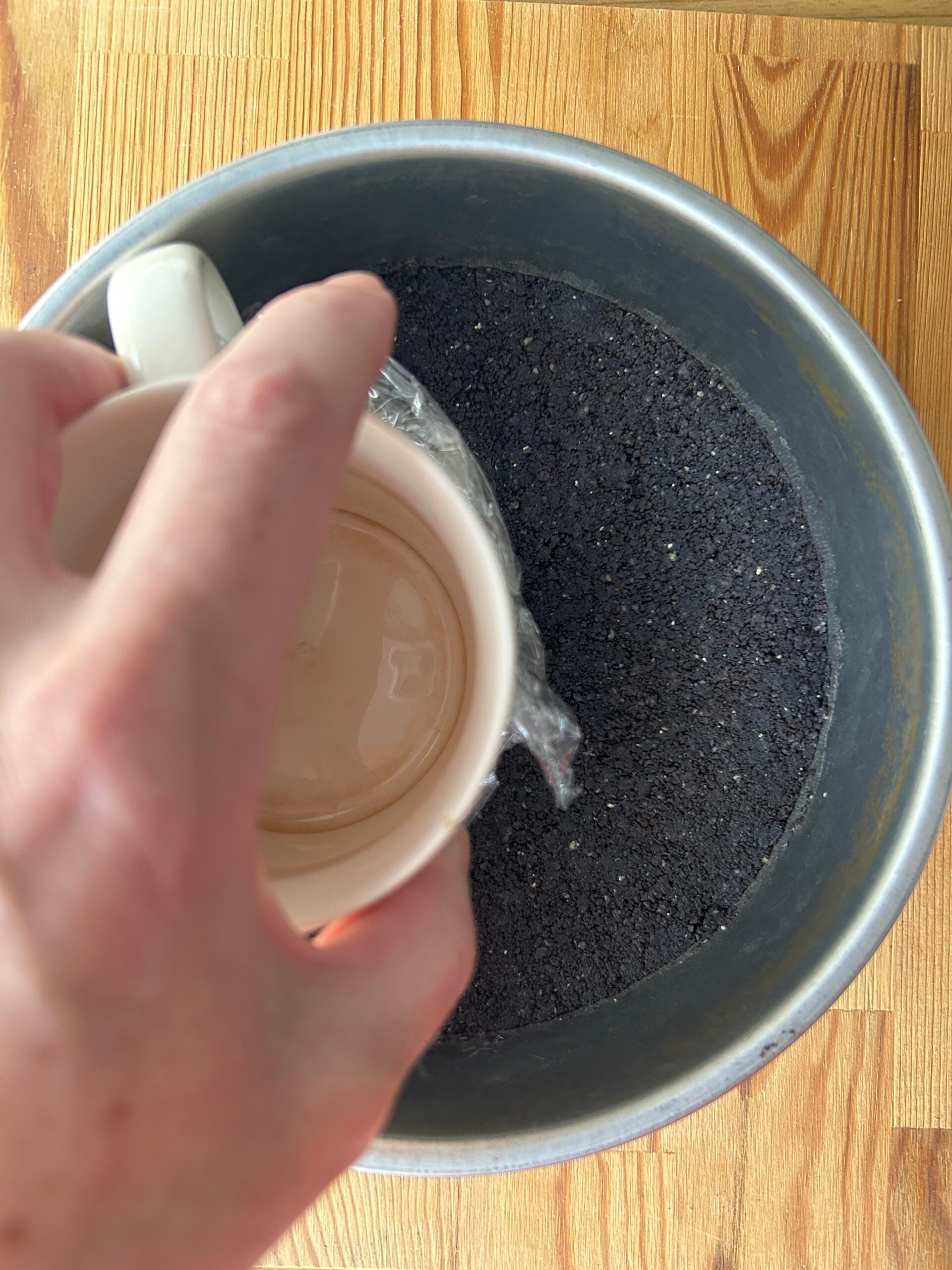 Pressing black sesame crust with a the bottom of a mug covered with plastic wrap.