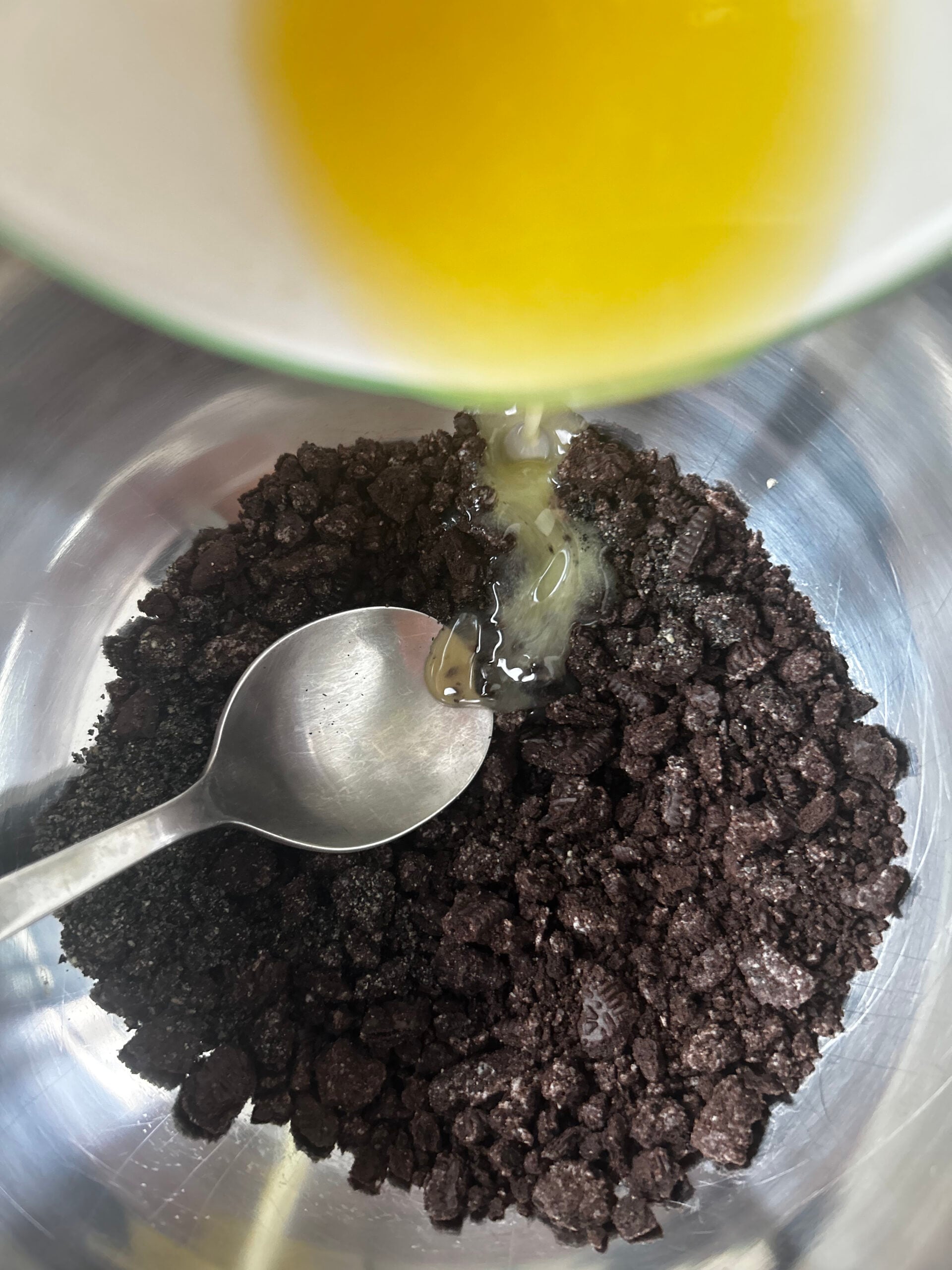Pouring melted butter on top of mix of crushed Oreo cookies and black sesame powder.